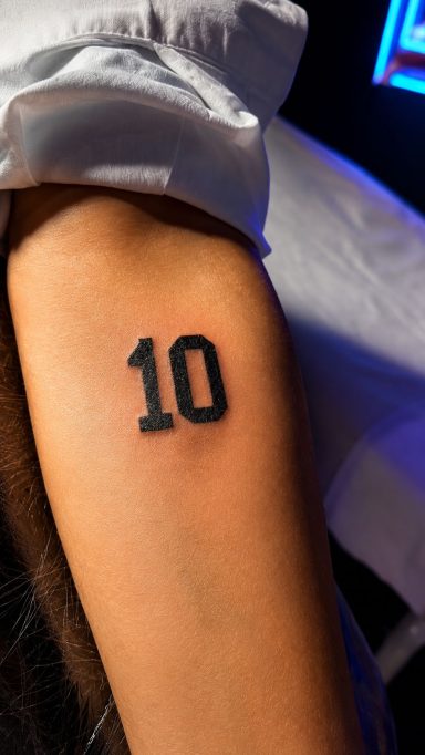 Tatuaje en el brazo que muestra el número "10" en color negro.